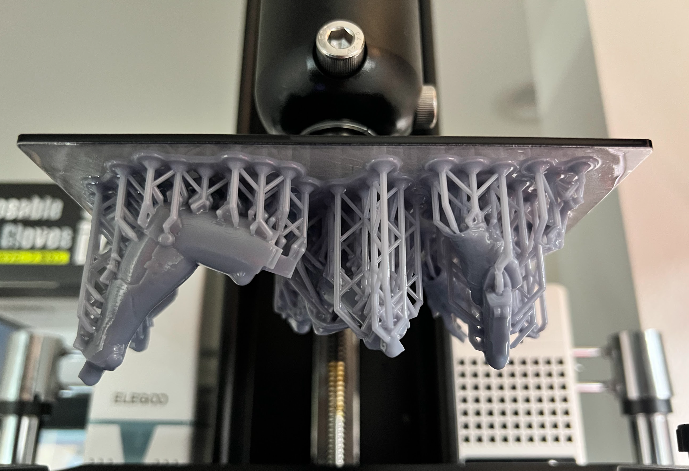 Supported resin model components suspended from a printer build plate.